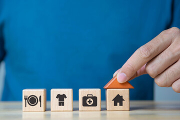 The investor's hand placed a wooden cube with food Clothing, housing, medicine, four basic human needs concept.