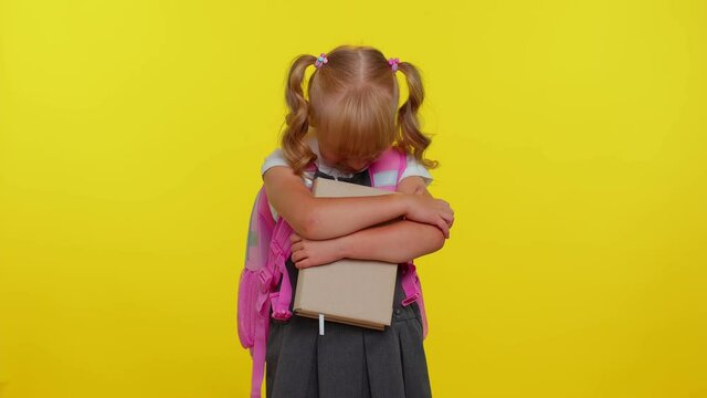 Upset disappointed blond teenage schoolgirl kid in uniform wipes tears and cries from despair, being sad because of unfair things on yellow studio background. Teenage education, back to school, study