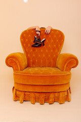 Tired woman holding shoes behind the sofa..While standing behind the yellow sofa. Photo in studio....