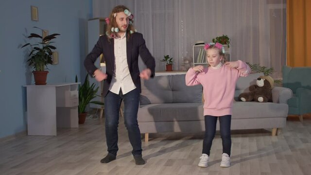 Cheerful Male Parent And Little Joyful Girl Have Fun Playing And Dancing Together In Curlers