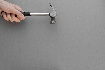 A hand holds a construction hammer on a gray background