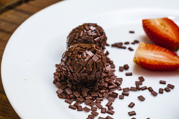 Brigadeiro, a traditional Brazilian sweet made with chocolate with sprinkles and strawberries, on a white plate.