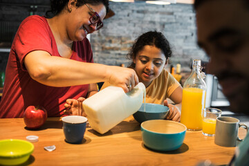 Mom pouring milk in daughter's cereal