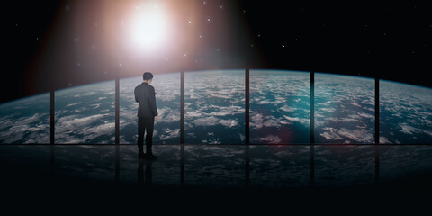 Fototapeta premium Concept of a successful business leader. A businessman stands near a panoramic window on the background of the sunlit world. with space to copy for business. Elements of this image furnished by NASA