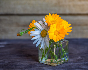Summer bouquet with chamomiles and calendula in a glass jar on the table