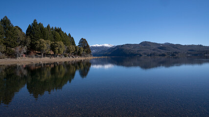 Fototapeta premium Summer day in the alps. The perfect reflection of the blue sky, green forest and mountains in the lake's water surface. 