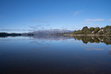The lake in a sunny morning. Panorama view of the forest, lake and the perfect reflection of the sky in the blue water. The Andes mountain range in the background.