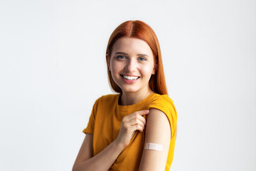 Covid-19 vaccinated caucasian smiling young woman showing arm with plaster and looking at the camera - obrazy, fototapety, plakaty