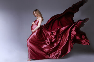 Pregnant girl in red dress. beautiful fabric texture on a light background