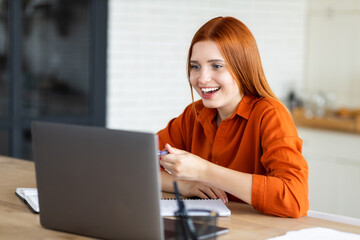 Young beautiful girl freelancer or student with red hair and casual clothes, studying remotely or...