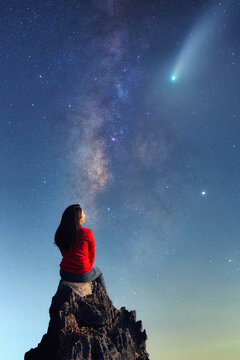 A young woman watching the beauty of the Milky Way and a meteor on the rocks. © 24Novembers