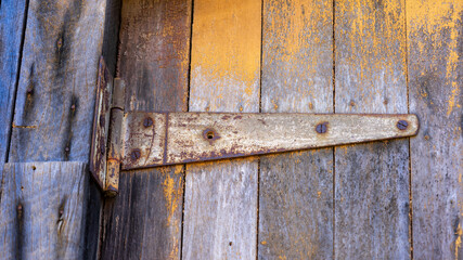 Metal hinge on an old wooden door with weathered yellow paint