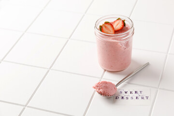one strawberry dessert mousse in glass with spoon on white board on white tile background