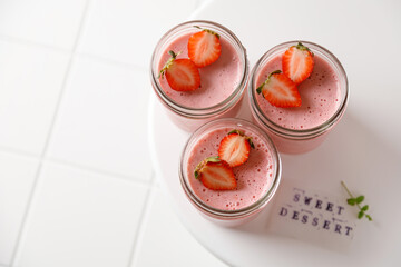 three strawberry desserts mousse in glass with sticker and mint on white board on white tile background