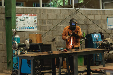 Hombre soldando en un taller con protección para el rostro y sus cuerpo 