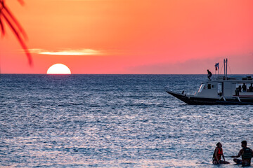 Naklejka premium Boracay, Philippines - Jan 21, 2020: Sunset on the background of bottles standing on the bar. The sun passes through the bright glass of the bottles. Background image for the screensaver.
