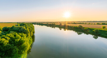 Fototapeta na wymiar Scenic view at beautiful summer river sunset with reflection on water with green bushes, grass, golden sun rays, calm water ,deep cloudy sky and glow on a background, spring , evening landscape