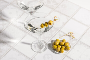 Martini cocktail with olives on the tiled table. An alcoholic classic drink with ice in an elegant glass