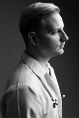 Young handsome man doctor with blond hair against gray background