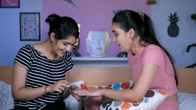 An Indian girl wearing a black printed T-shirt applying nail polish on her best friend's hand. College-going student - beauty treatment. Nail polish tattoo. Indian siblings  Young sisters
