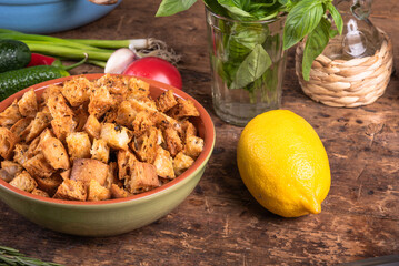 Clay bowl with homemade croutons on the table with ingredients for vegetarian salad, tomatoes, lemon, cucumbers, basil and onions