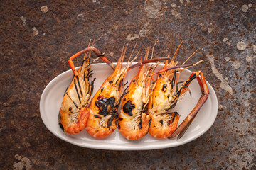 grilled giant freshwater prawns in oval ceramic plate on rusty texture background, top view, river...