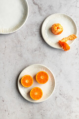 Peeled and sliced mandarins in ceramic plates on marble surface