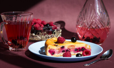 a piece of raspberry's cake with curd or cheese filling on blue plate closeup,  berry's compote on dark purple background