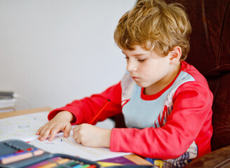 Portrait of cute happy school kid boy at home making homework. Little child writing with colorful pencils, indoors. Elementary school and education. Kid learning writing letters and numbers