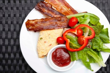 Western breakfast, scrambled eggs, bacon and fresh vegetables with tomato sauce