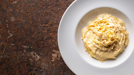 spaghetti carbonara with cream sauce in white ceramic plate on rusty texture background, copy space...