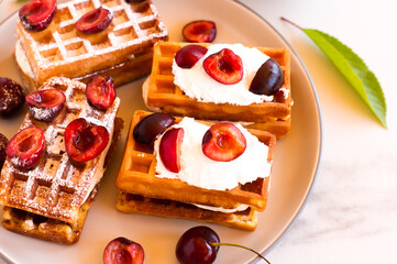 Belgian waffles on a plate with juicy cherries and yogurt. delicious healthy breakfast.