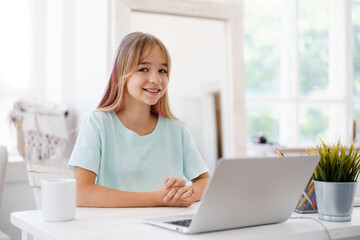 Fototapeta premium Happy little girl pupil using laptop at home