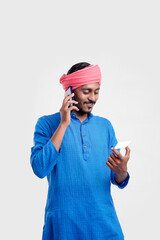 Naklejka premium Young indian man in traditional wear and talking on smartphone and using card over white background.