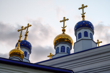 Fototapeta na wymiar Blue domes with gold stars of the ancient Church of the Ascension in the village of Bolshie Brusyany (Ural, Russia). Close-up of a golden dome. White brick air church. The legacy of ancestors. 