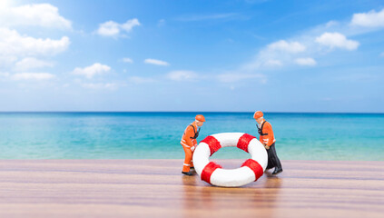 Miniature worker in safety suit with lifebuoy over blurred beach background, summer outdoor day light, life insurance concept, life guard