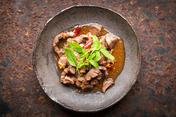 Pad Ka Prao Kruang Nai Gai, Thai food, basil stir fried chicken offal, variety meats, pluck or organ meats in wabi sabi style plate on rusty texture background, top view