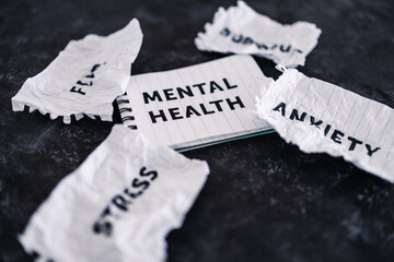 Mental health text on notepad surrounded by Fear Anxiety Stress and Burnout words on scrunched up...