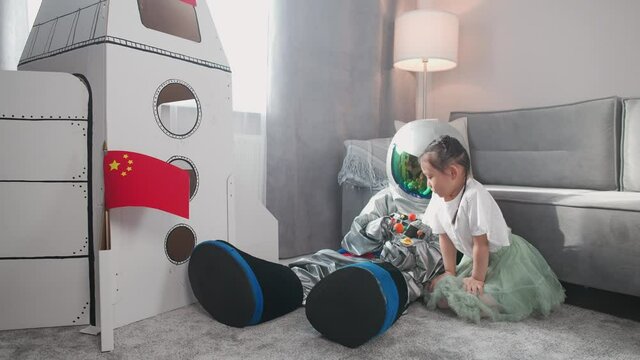 Asian kids play in the living room at home, a boy in an astronaut costume sitting on the floor with her sister, kids playing with a toy model of the solar system, 4k slow motion.