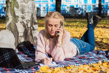 Young woman working with laptop outdoors and talking on the phone