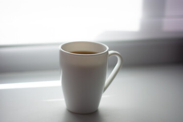 white mug of coffee by the window in the morning