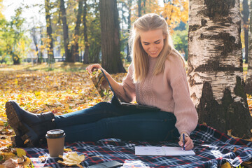 Young woman working with laptop outdoors and making notes in notepad