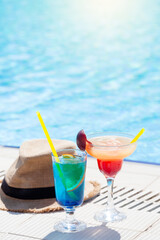Two colorful cocktail glasses at the edge of swimming pool