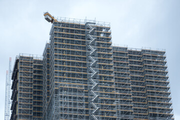 Fototapeta premium Scaffolding and metallic equipment around a high-rise building construction. No people, day light, outdoors.