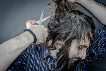 portrait of a young man with a beard and long hair who, with a scissor in his hand, wants to change his look and wants to cut his hair, concept to illustrate the desire to change