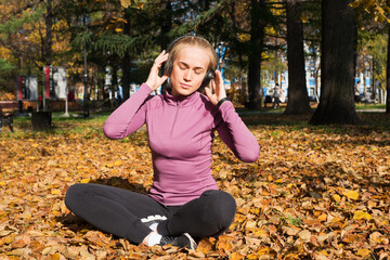 A young woman plays sports outside in an autumn park and listens to music with headphones