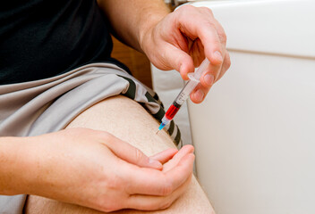 Close up view of man person do the B12 vitamin injection shot in home itself to himself in leg(...