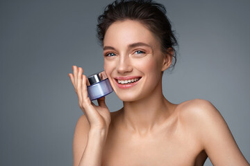 Beautiful woman with jar of moisturizer cream. Photo of woman with perfect skin on gray background. Beauty and Skin care concept