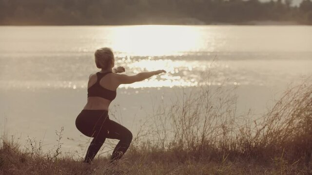 Fit Sporty Woman Squats Exercising At Sunset. Stretching Fitness Workout Activity. Squats Workout Practicing. Sport Recreation Healthy Lifestyle. Warming Up Aerobic Exercises. Cardio Squat Training. 