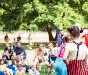 The girls in clown costumes have a performance in front of a large number of people in the park, on the street. Theater outside. Teenage girls entertain the audience with colorful costumes